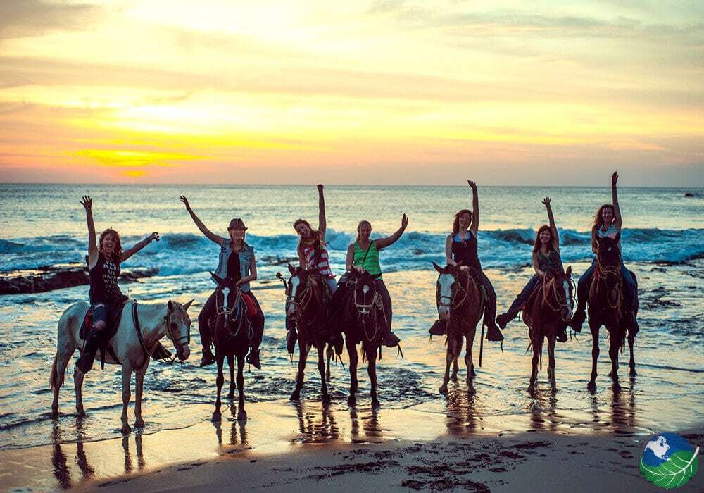 Riders on horseback on a Pacific beach at sunset